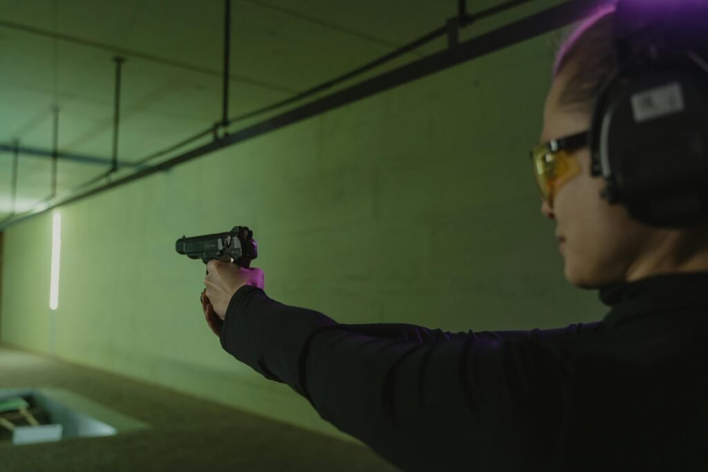 Focused woman at an indoor shooting range practicing target shooting with safety gear and a handgun.