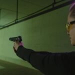 Focused woman at an indoor shooting range practicing target shooting with safety gear and a handgun.